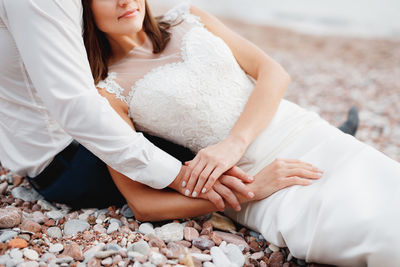 Midsection of couple sitting on pebbles at beach