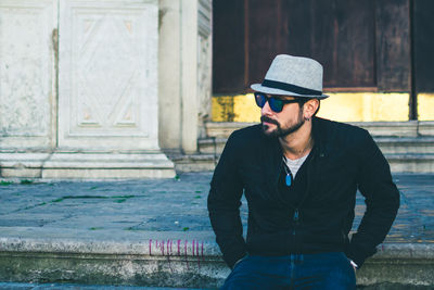 Young man wearing hat while standing against built structure