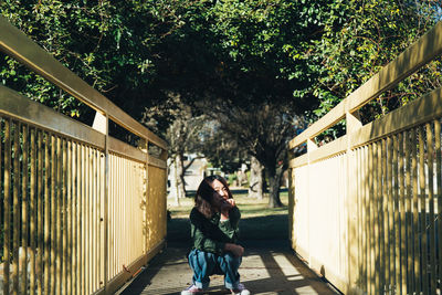 Portrait of woman crouching on footbridge against trees
