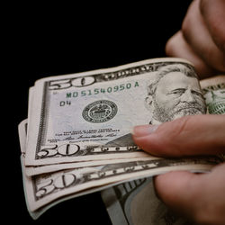 Cropped hand of person holding paper currency against black background