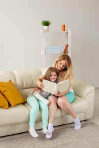 Full length of young woman using phone while sitting on sofa at home