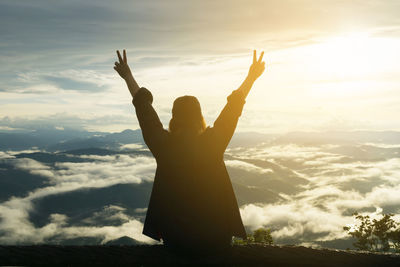 Man with arms raised against sky during sunset