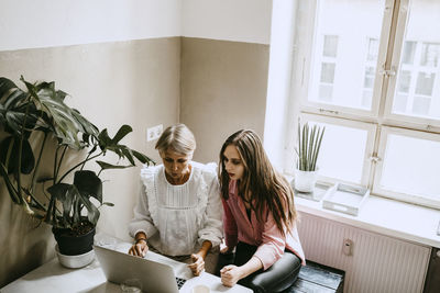 Female coworkers using laptop while sitting in office