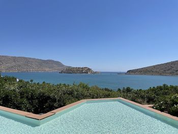 Swimming pool by sea against clear blue sky