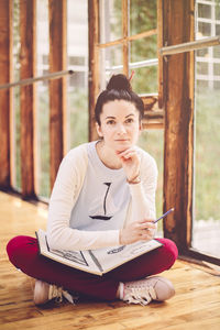 Portrait of woman with book sitting on hardwood floor at home