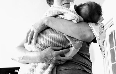 Midsection of mother holding baby wrapped in towel while standing at home