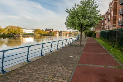 Footpath by canal against sky in city