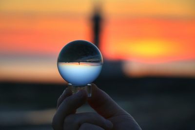 Close-up of hand holding crystal ball against sunset sky