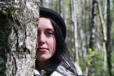 Portrait of woman against tree trunk in forest