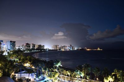 Illuminated cityscape by sea against sky at night