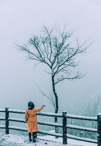 Man standing by bare tree against sky during winter