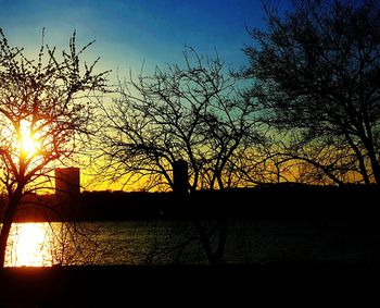 Silhouette bare tree by lake against sky during sunset