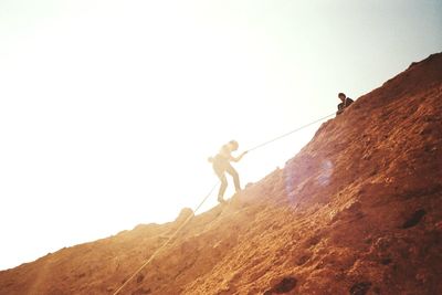 Low angle view of person climbing rocky mountain against sky