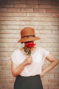 Woman with red rose standing against brick wall