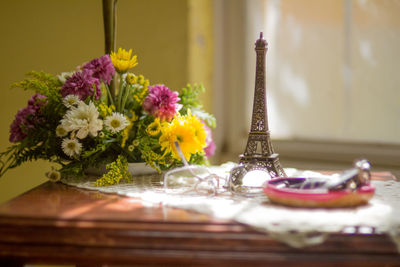 Miniature eiffel tower by eyeglasses and flower vase on table