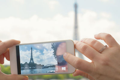 Cropped image of hands photographing eiffel tower through mobile phone