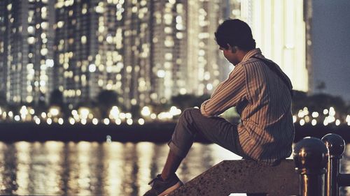Side view of young man sitting in city at night