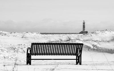 Empty bench on snow covered field against sky