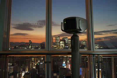 Illuminated buildings against sky during sunset seen through glass window