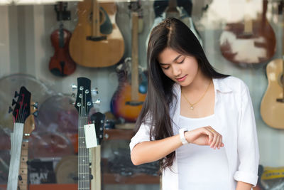 Young woman checking time while standing against guitar store