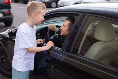 A cute child accompanies a happy father to work. dad is sitting in the car. give five