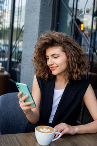 Young pretty curly haired business woman talking by smart phone in cafe. social media concept