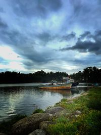 Boats in calm lake against cloudy sky