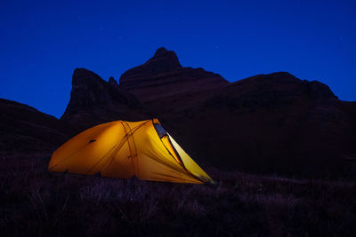 Yellow tent on field against mountain at night