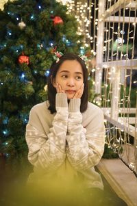 Portrait of young woman standing against christmas tree