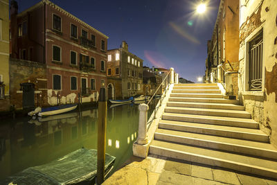 Steps on footpath by canal amidst buildings in city at dusk