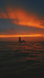 Silhouette young woman surfing on sea against cloudy sky during sunset