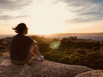 Man sitting on rock looking at sunset