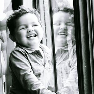 Cute boy laughing by window at home