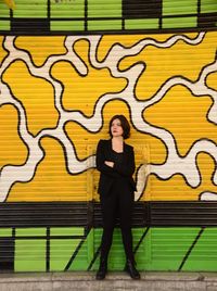 Thoughtful young woman standing against yellow shutter