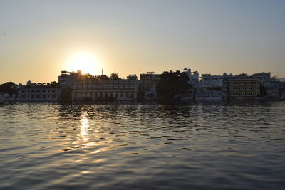 Buildings by river against sky during sunset