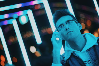 Close-up of thoughtful man wearing eyeglasses against lights at night