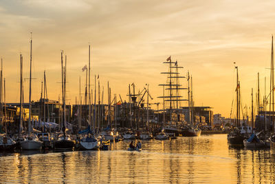 Sailboats moored at harbor against sky during sunset