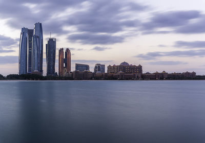 Sea and buildings in city against cloudy sky