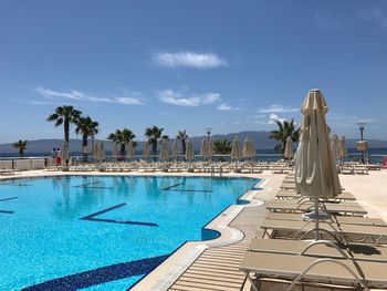 Swimming pool by palm trees against blue sky