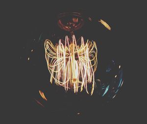 Close-up of illuminated light bulb hanging against black background