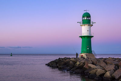 Lighthouse by sea against sky during sunset