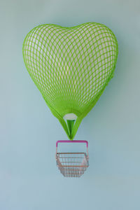 A heart shaped balloon with a stretched green grocery net and a tied grocery basket.