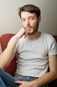 Portrait of young man sitting with hand on chin at home