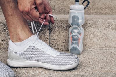 Low section of man tying shoe by water bottle on steps