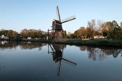 Traditional windmill by lake against clear sky