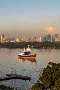 Boats in river against buildings in city at sunset