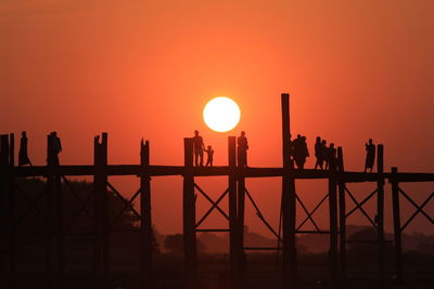 Silhouette people on u bein bridge over river during sunset