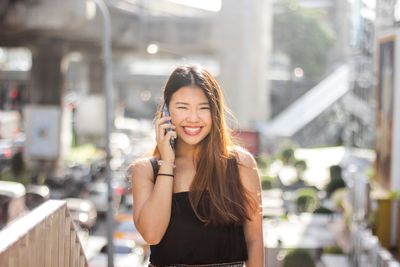 Young woman using smart phone while standing on laptop