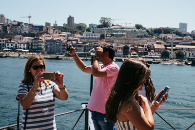 Woman photographing in city at sea against sky