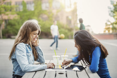 Side view of female teenagers using digital tablet at table outdoors